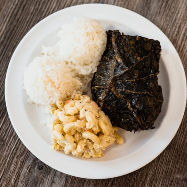 A Hawaiian plate lunch with lau lau, white rice, and macaroni salad on a white plate.