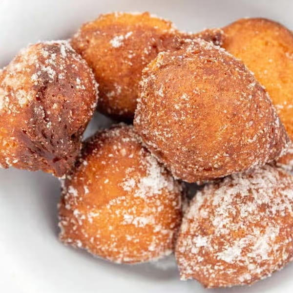 Close-up of golden-brown Hawaiian malasadas, sugar-dusted doughnuts, in a white bowl.