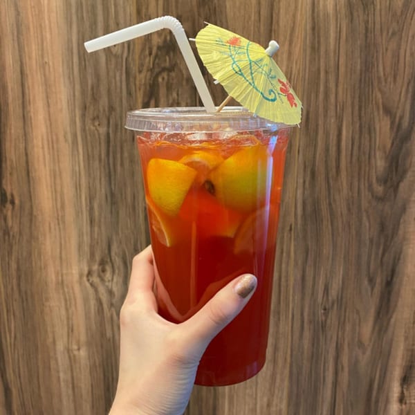 Hand holding a vibrant red Hawaiian drink with lemon slices, a straw, and a small yellow umbrella.